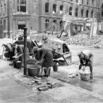 German women doing their washing at a cold water hydrant in a Berlin street. A knocked out German scout car stands beside them. photograph No. BU 8609 from the Imperial War Museum collection No. 4700-30